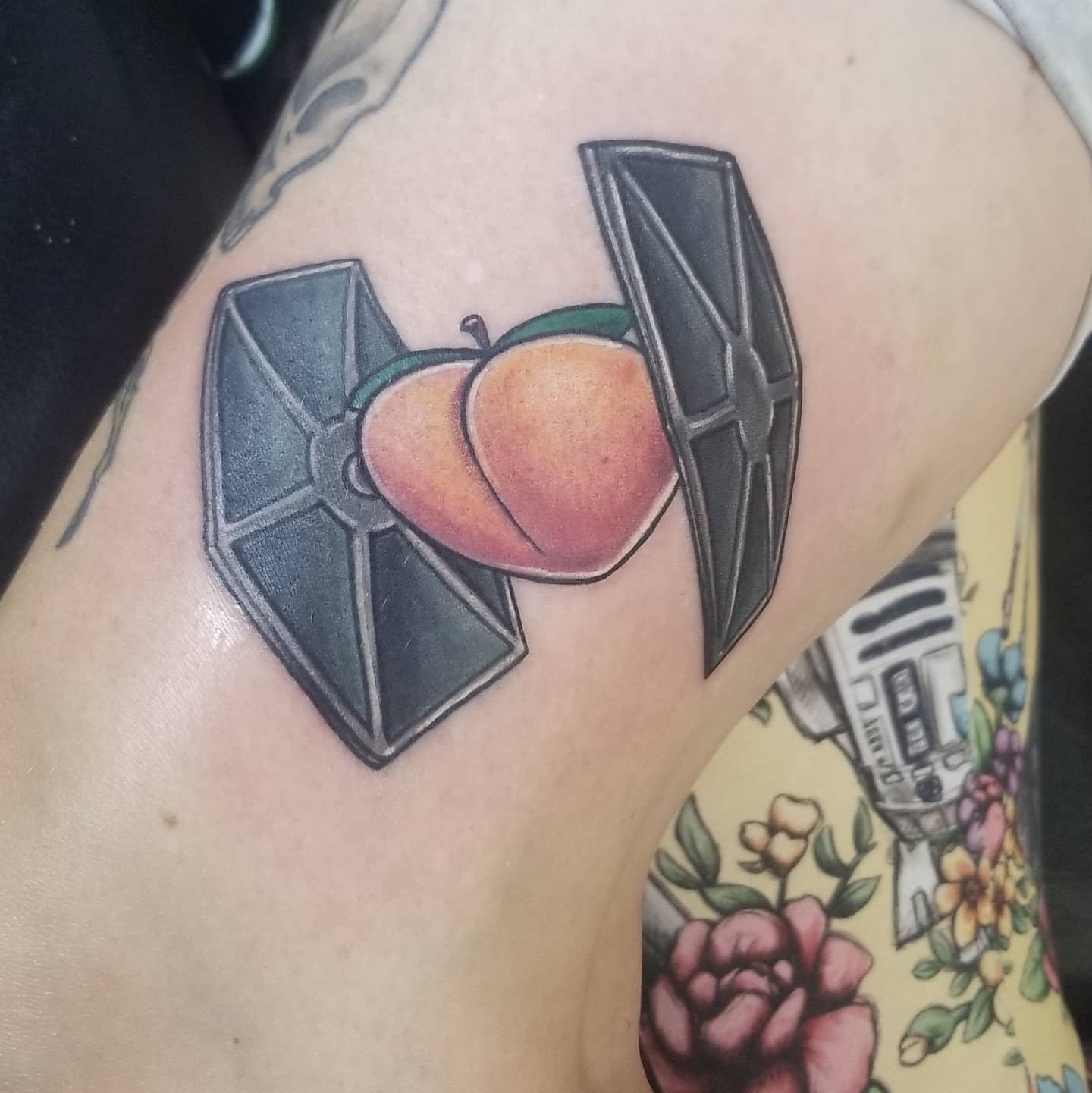 Colorful tattoo of a peach held between the wings of a TIE fighter from Star Wars